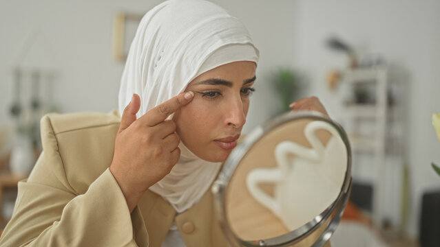 Woman touching eyebrows and temples while inspecting skin in mirror in studio; self care contemplation.