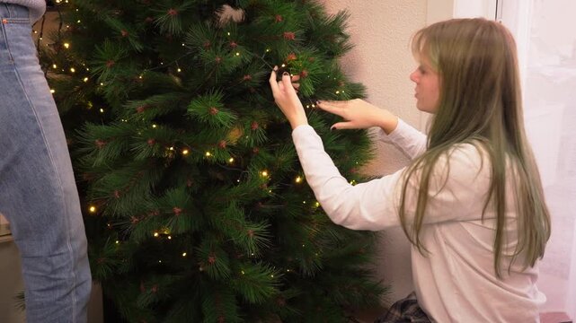 Woman decorating an artificial fir tree with glowing string lights at home, creating a warm and inviting interior for winter celebrations and seasonal holiday gatherings