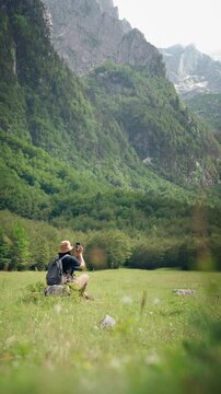 Female hiker using a smartphone while resting in a meadow during a hiking trip with a scenic mountain view, combining outdoor adventure, navigation and digital connectivity.