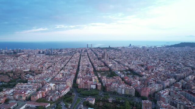 Aerial drone slowly pulling back over Barcelona Eixample grid with Mediterranean sea on the horizon at dusk, Spain