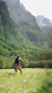 Female hiker taking photos with a professional camera while exploring a scenic forest with mountain views, combining hiking, travel and nature photography.