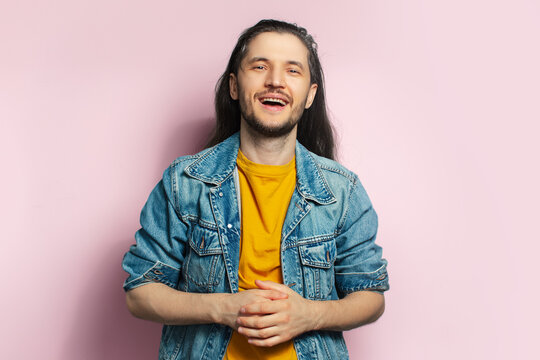 Portrait of excited happy young man with long hair on pastel pink background.
