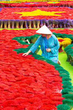 A woman in a conical hat among colorful incense sticks. Tam Coc, Vietnam.