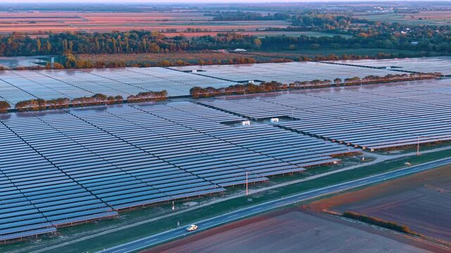 Solar power field near road during soft dusk. Aerial perspective captures large solar panels beside country road with car.