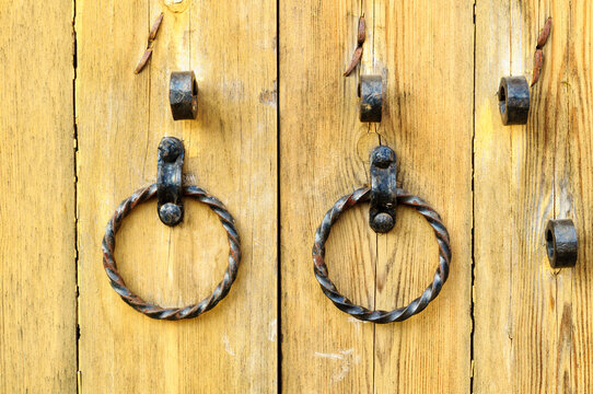 Rustic texture background with old twisted iron rings hanging on weathered wooden door planks and dark metal brackets above them