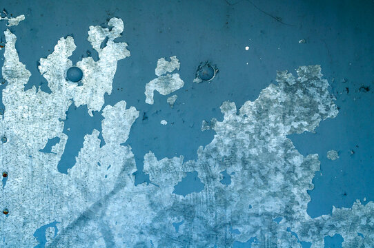 Texture background with peeling blue paint on a metal surface and large grey flaking patches revealing the rough underlayer beneath