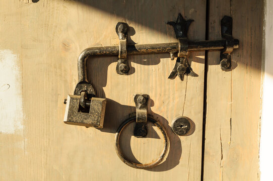 Rustic texture background with an old metal latch, padlock and iron ring mounted on a weathered wooden door in warm sunlight