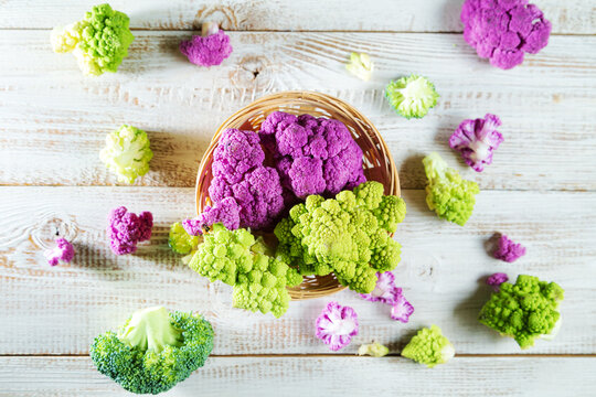 Multicolored cauliflower in a wicker basket on a wooden table.