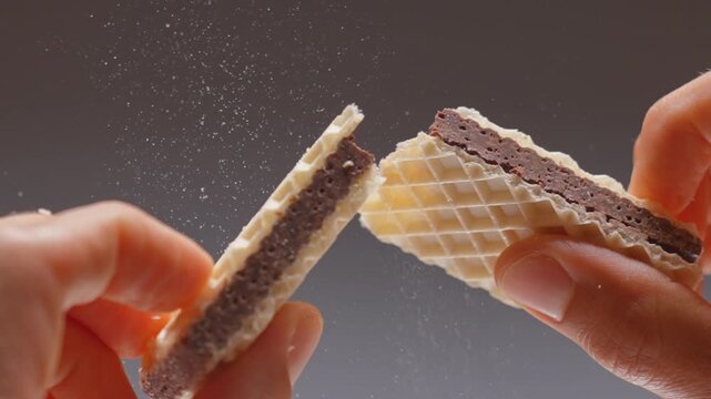 Crispy wafer bar snaps in half with flying crumbs during detailed macro slow motion inside studio. Cinematic chocolate dessert video footage provides dynamic textured asset for design element.