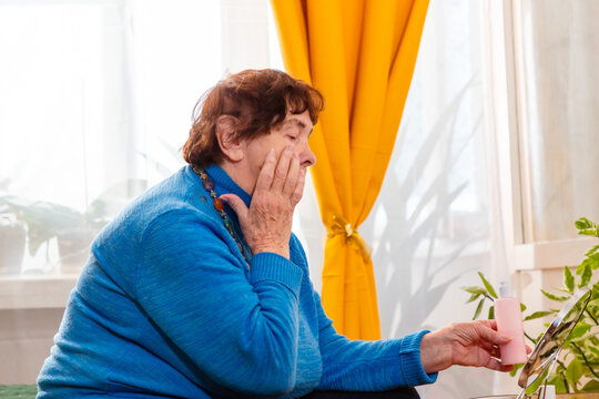 Senior female using facial cream and lipstick indoors. Healthy skin and confidence. Concept of mature beauty.