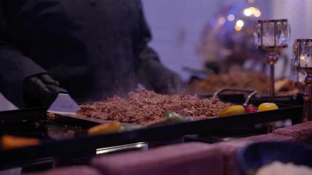 Professional chef cooking shredded meat on a hot flat top grill at a catered event dinner party