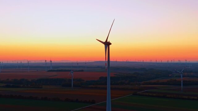 Wind generator silhouette in field during golden sunset. A central turbine operates above vast farmland under a clear evening sky.