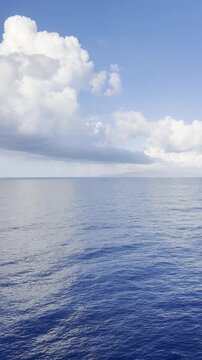 Vertical view of calm deep blue Mediterranean Sea with a large cumulus cloud and a distant island on the horizon, from a cruise ship