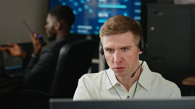 Caucasian young adult specialist wearing headset talking while monitoring data in cybersecurity office. Suitable for software support advertising or cyber defense video projects