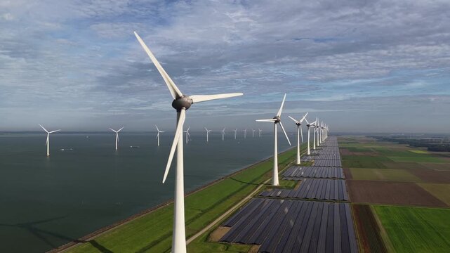 Wind turbines and solar panels on a lakeshore producing sustainable energy seen from above.