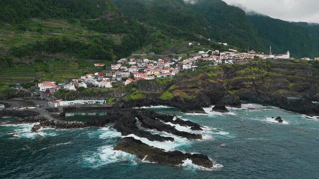 Lava reefs and coastal cliffs at Seixal, Madeira, Portugal, aerial view. Village stands above volcanic shoreline beside Atlantic Ocean