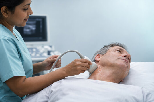 A female doctor uses an ultrasound probe to examine the neck of a senior man lying on a medical bed in a clinic.