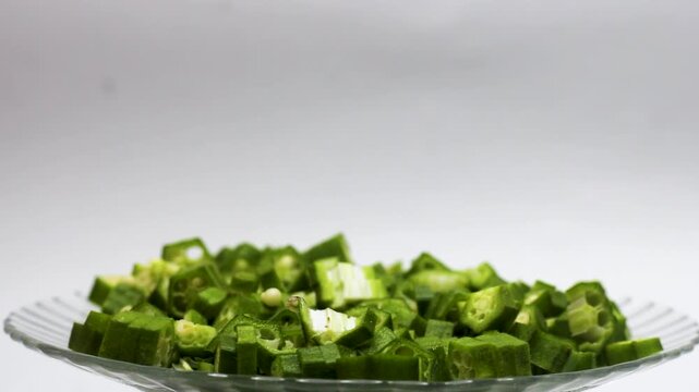 Fresh chopped okra pieces rotating on glass plate isolated against white background.