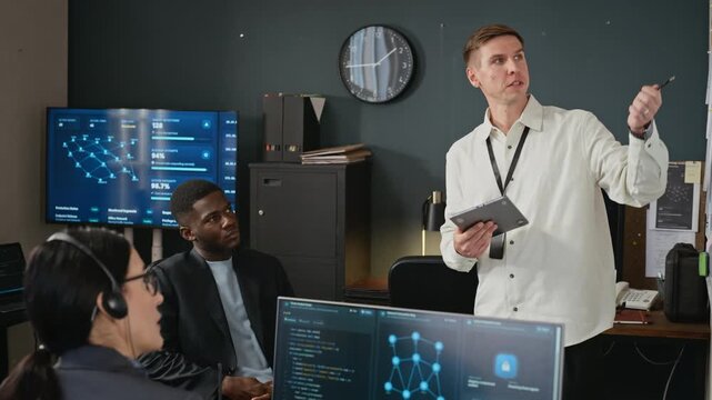 Caucasian specialist holding tablet and explaining network security data on whiteboard to diverse colleagues. Footage suitable for corporate training and technology marketing campaigns
