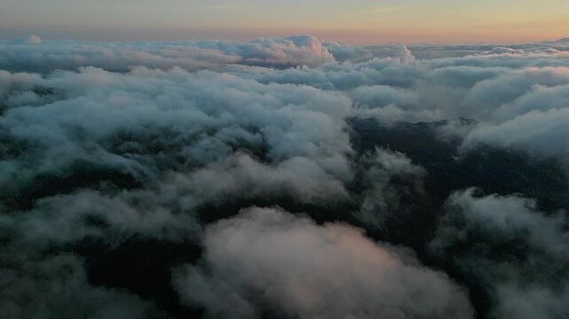 Layered clouds over dark mountain terrain beneath pink dawn sky. Transition from night to morning.
