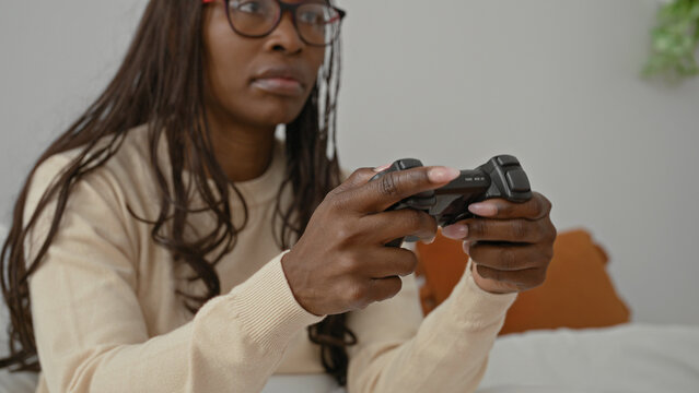 Woman gripping game controller while seated on bed in bedroom, hands visible on joystick and buttons; concentration.