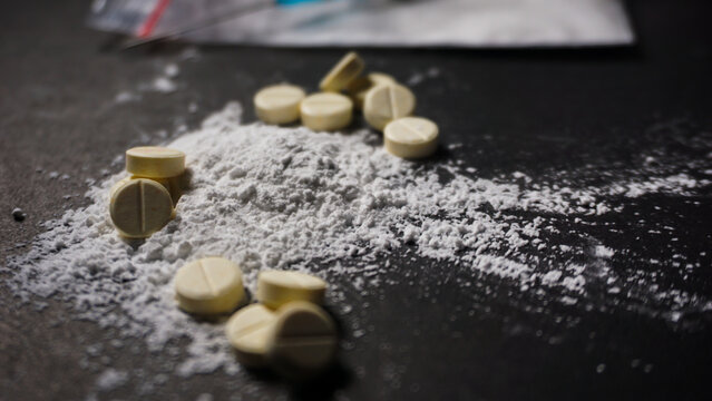 Close up white powder and some white pills on black surface. Concept of misused drugs. 