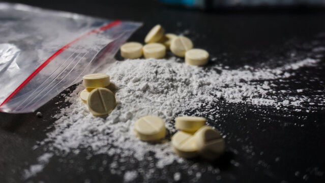 Close up angle of white powder spilled from medical plastic clip. Several pills, misused drugs concept. 