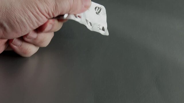 Hand examining and dropping an empty pill blister pack onto a dark table surface.