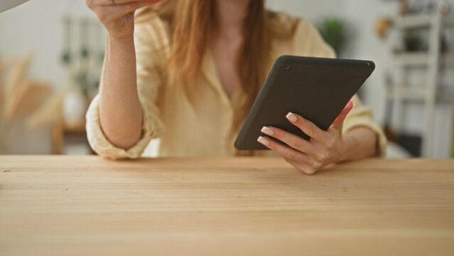 Woman holding tablet and reaching for red coffee cup on table in building; calm concentration morning routine.