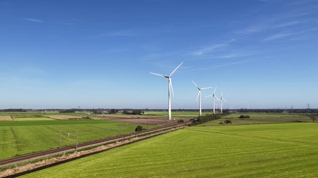 A passenger train of the Nederlandse Spoorwegen NS travels along wind turbines producing sustainable energy.