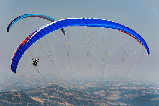 Paragliders in the air, pilots in flight, against the backdrop of an Italian landscape.