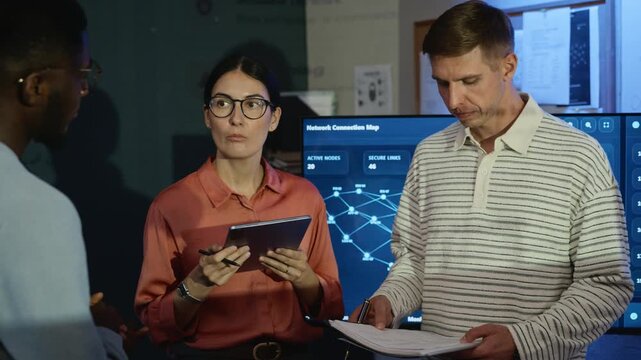 Diverse team of software specialists discussing network data using digital tablet in server office. Perfect for corporate cybersecurity training, data protection campaigns and technology advertising