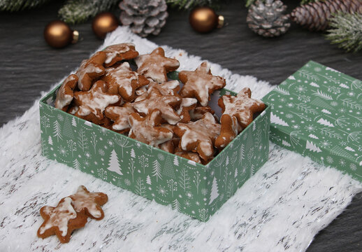  Sternf&ouml;rmige Lebkuchen mit Zuckerguss in einer gr&uuml;nen Weihnachtsschachtel auf wei&szlig;em Fell.
