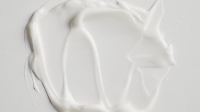 White cosmetic cream texture being spread with spatula on a white background creating a smooth smear