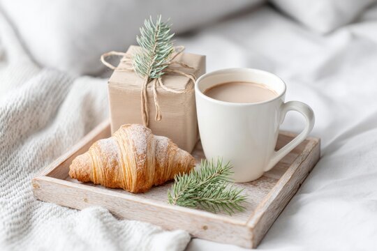 Cozy breakfast tray with wrapped gift, coffee, and croissant on soft white bedding