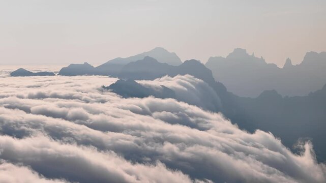 Mountain peaks above moving clouds. Aerial view of cloud cover around rocky ridges