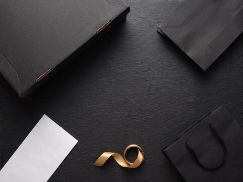 Flat lay black shopping bags, box and gold ribbon on dark slate