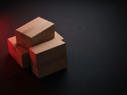 Stacked cardboard shipping boxes on dark background with red light