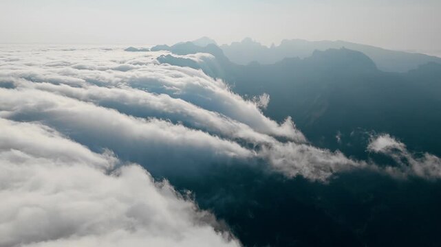 Cloud movement across mountainous terrain, aerial view. Dense clouds around ridges and over valleys