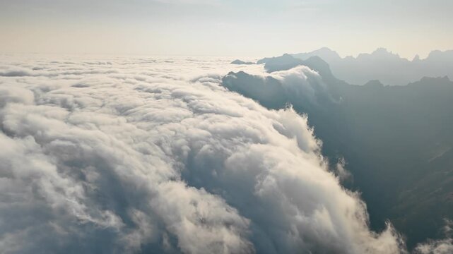 Clouds moving along mountain ridge above valley. Aerial view from above dense cloud layer.