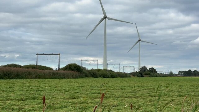 A yellow and blue intercity passenger train of the Nederlandse Spoorwegen NS travels along wind turbines producing sustainable energy.