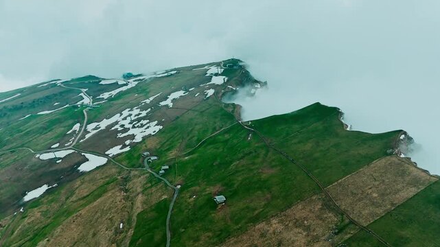 Seceda alpine plateau with scattered snow patches and low clouds, aerial view, Italy