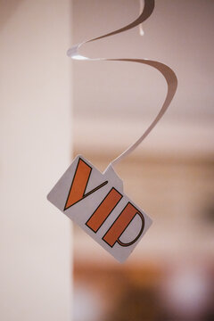  Close-up of a VIP tag suspended from a ribbon against a softly blurred neutral background, representing exclusive access, premium service and luxury events.