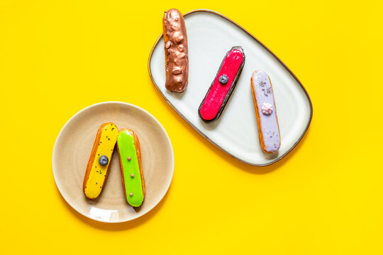 Elegant assortment of glazed eclairs on plates - gourmet pastry presentation with modern cafe aesthetic