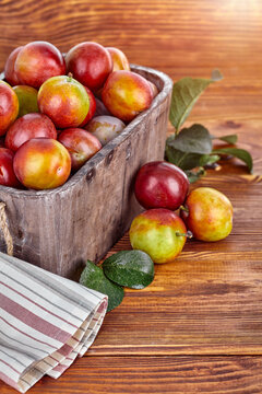 Fresh plum fruits in rustic wooden basket with green leaves. Autumn harvest crops on the old wood table background