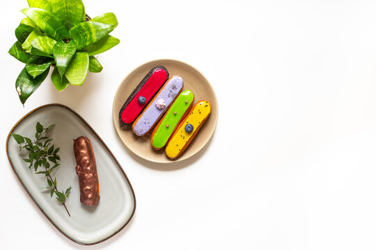 Assorted French eclairs with chocolate, berry and mint icing on plates. Elegant sweet food background, top view