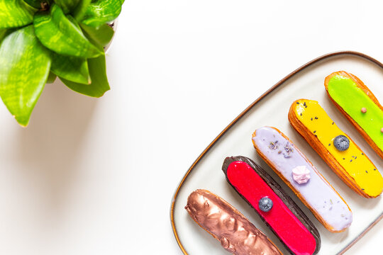 Colorful gourmet eclairs with glazed topping on plate - modern pastry flat lay in soft natural light, top view dessert concept