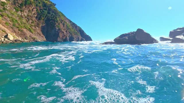 Turquoise surf rolling toward rocky coastal cliffs, water level view