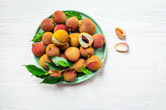 Fresh lychee fruit with green leaves on a plate, top view