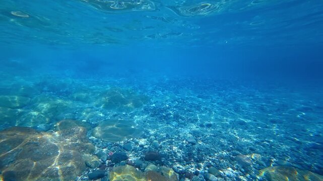 Underwater view of clear blue sea with rocky seabed and sunlight reflections
